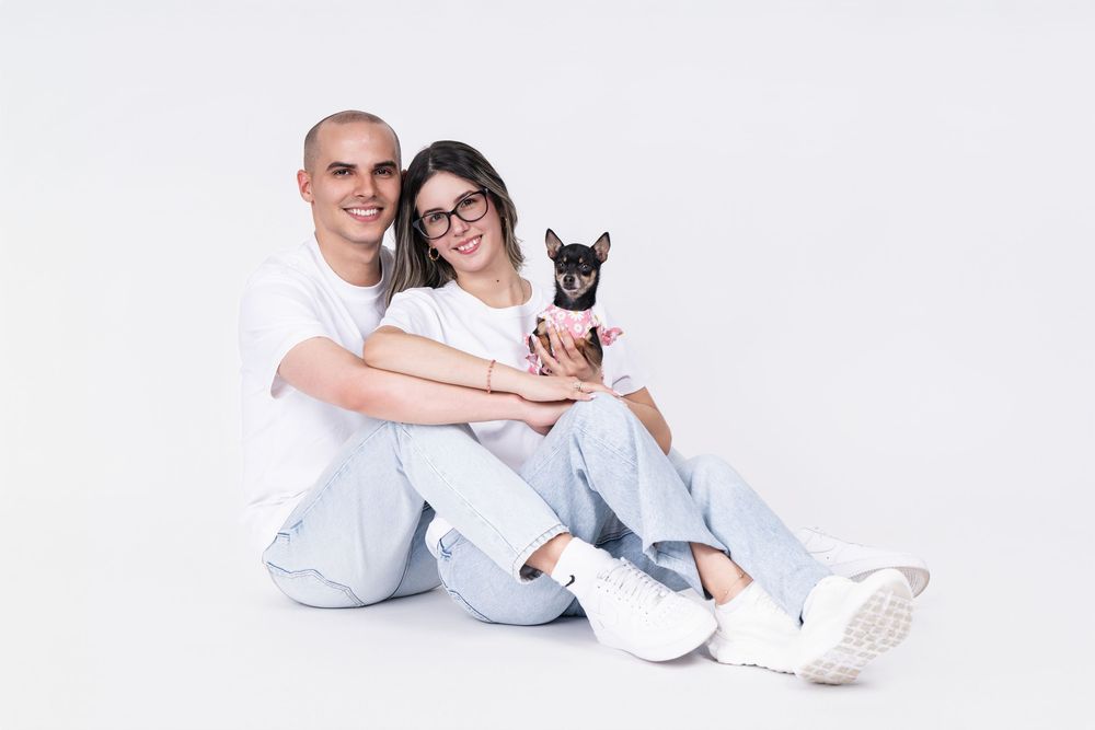 Happy couple in matching outfits sitting with their small chihuahua on white background.