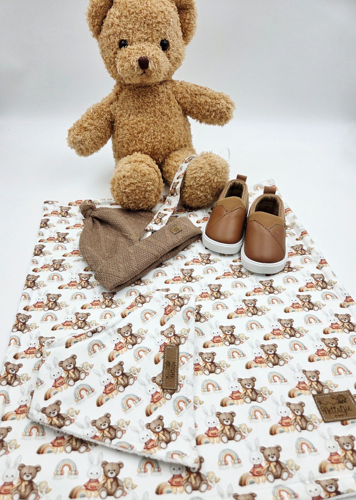 Teddy bear plush toy sitting on brown bear print baby blanket with leather shoes.