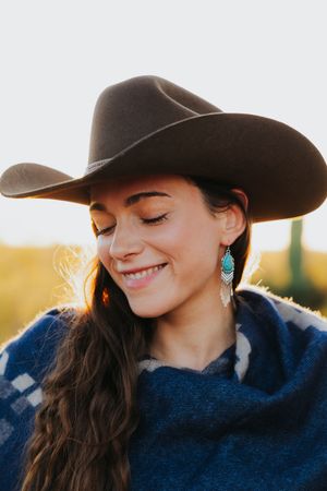 Candid western style portraits with turquoise earrings and cowboy hat in warm sunlight.