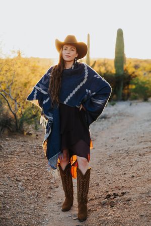 Western fashion shoot featuring a blue poncho and cowboy boots against desert landscape.