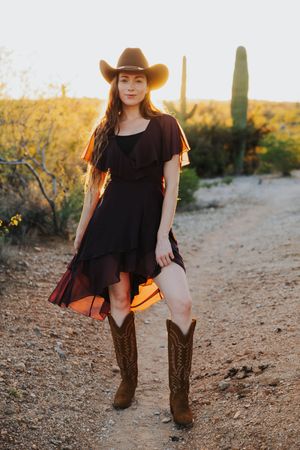 A western-styled outfit featuring a black dress and brown cowboy boots photographed in a desert setting.