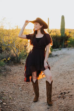 A western-inspired desert photoshoot featuring cowboy boots and hat against a backdrop of saguaro cacti.