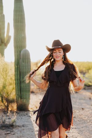 Dancing in black dress among desert cacti during sunset photoshoot.