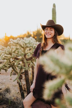 A desert fashion portrait with cowboy attire surrounded by cholla cactus and saguaros at sunset.