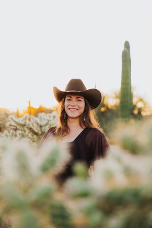 A desert portrait with western wear surrounded by desert plants during sunset.