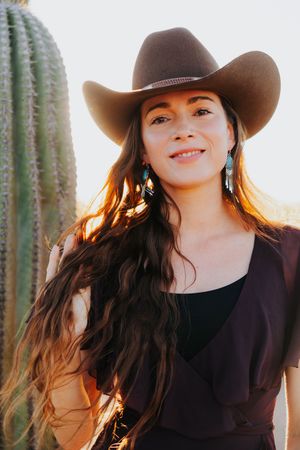 Sunset portrait with cowboy hat and black dress against desert cactus backdrop.