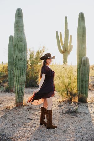 Western boots and black dress ensemble photographed among majestic saguaro cacti.