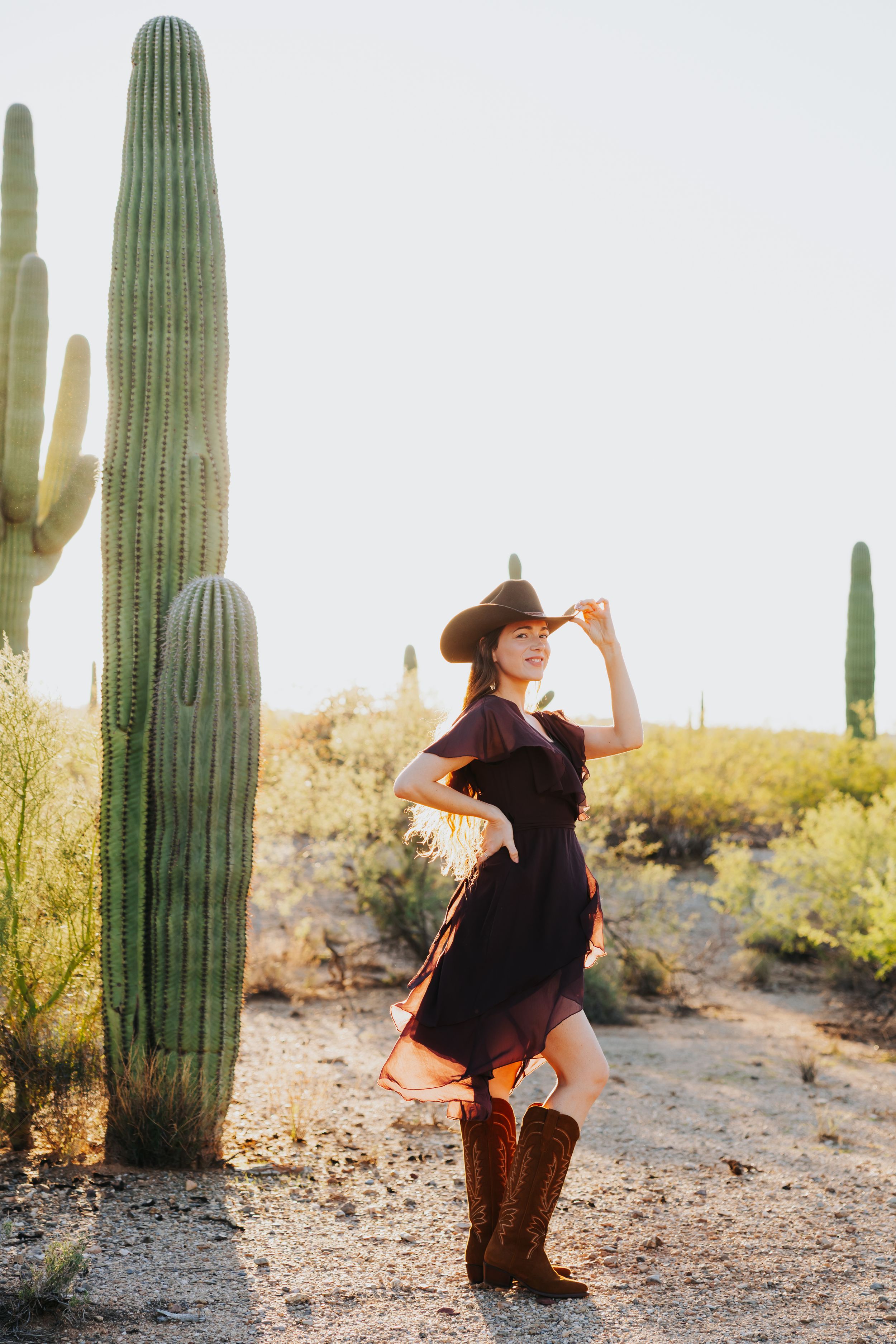 Woman in western attire dances in desert setting surrounded by majestic saguaro cacti.