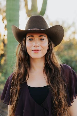 A western-themed portrait session featuring a brown cowboy hat and black outfit against saguaro cacti.