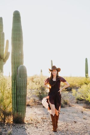 Dancing figure in western wear performs against backdrop of towering desert cacti.