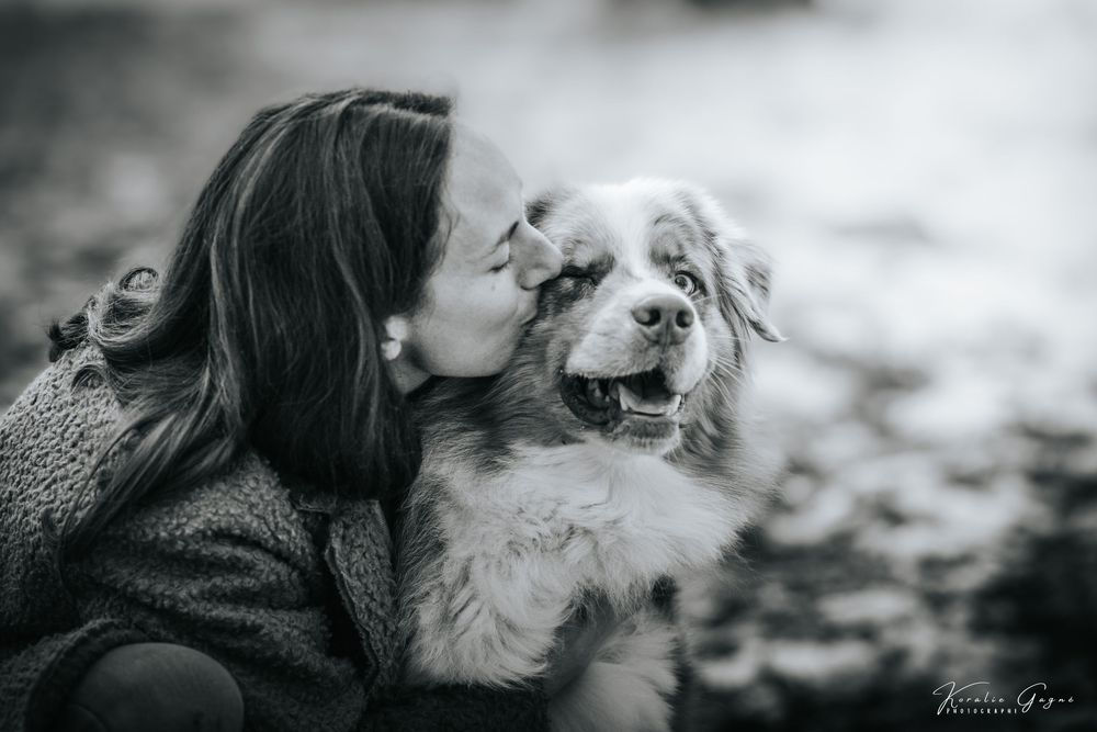 A woman in a dark coat embraces a dog, likely a golden retriever, in a snowy forest.