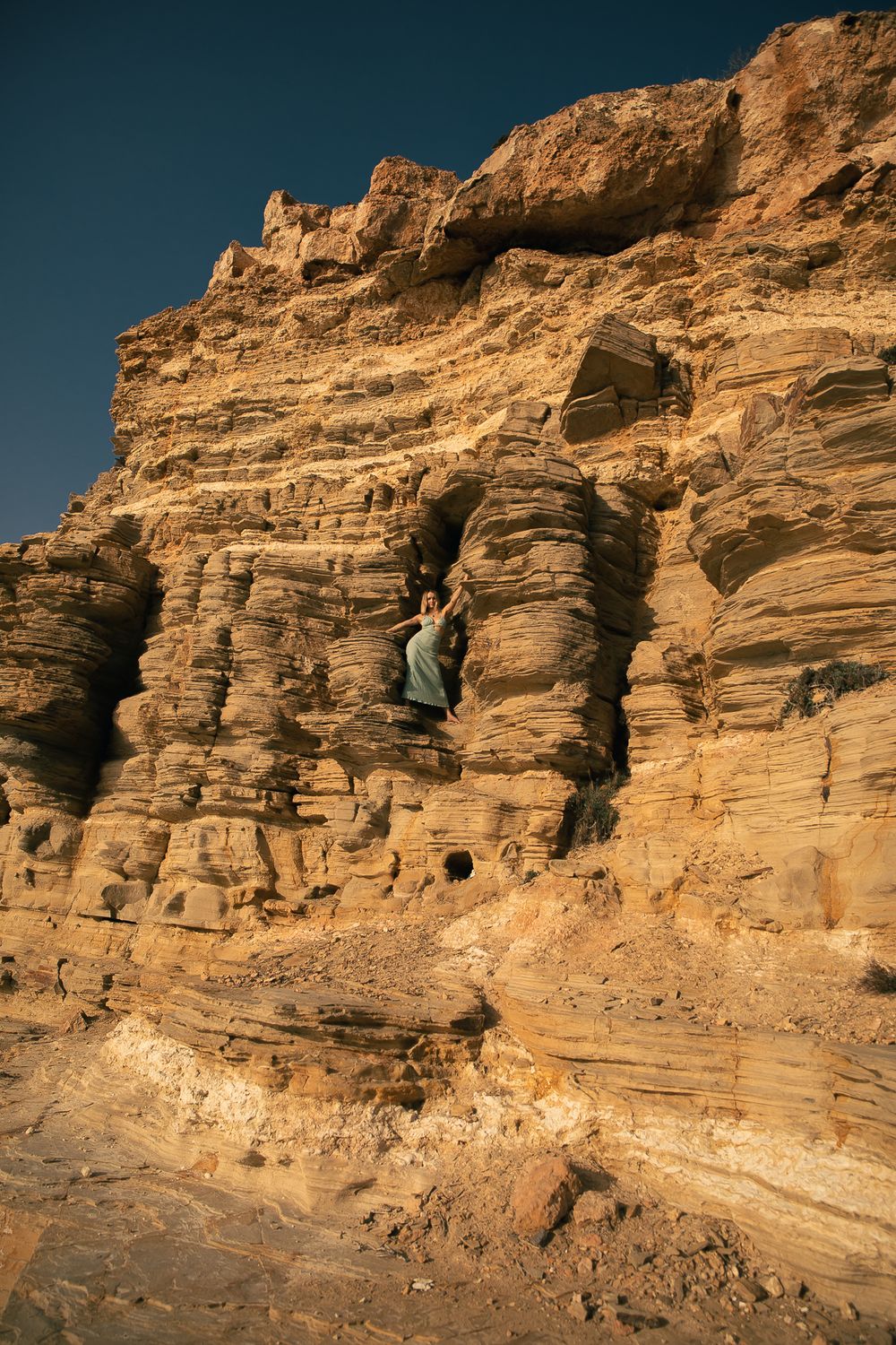 Rugged desert canyon landscape with layered sandstone formations under blue sky.