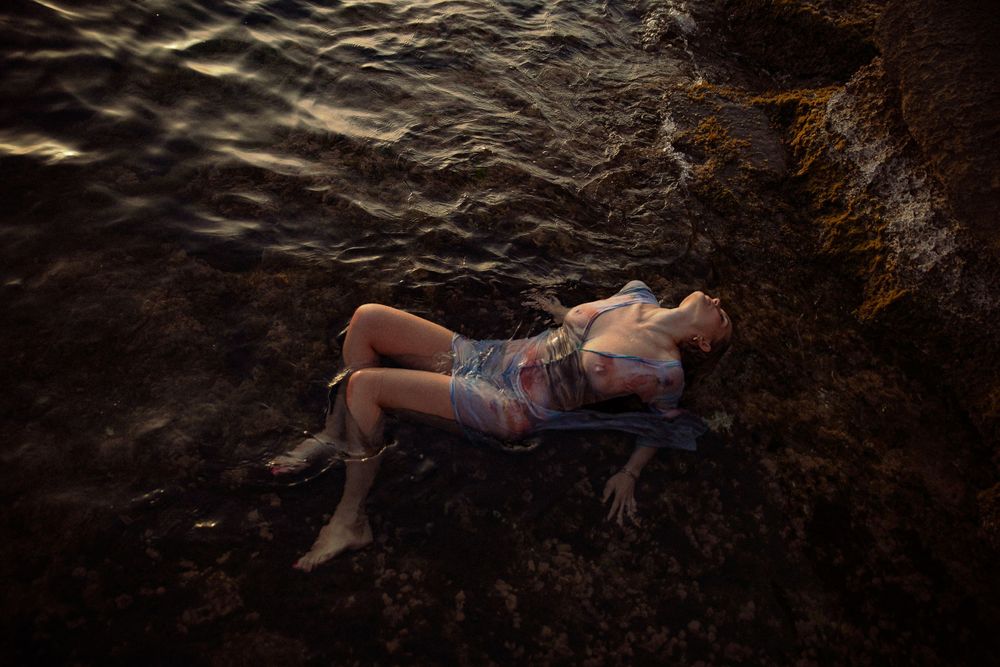 Person lying on dark rocky surface in artistic pose.