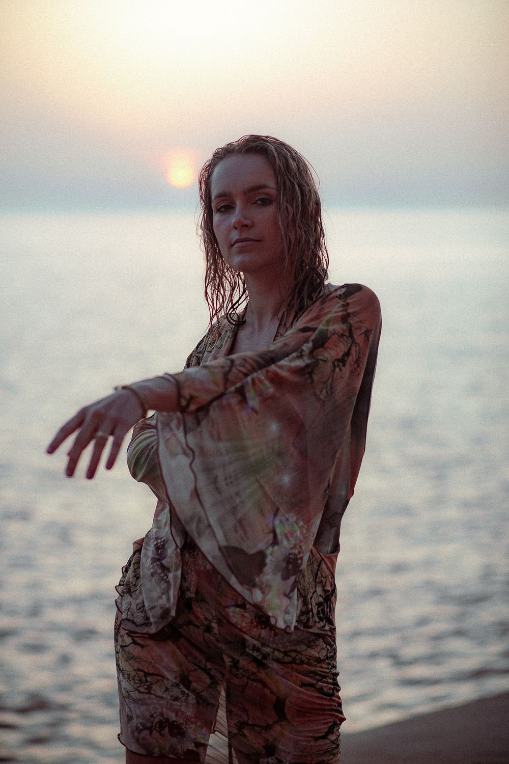 Artistic portrait of someone in wet clothing posing dramatically at beach during sunset.