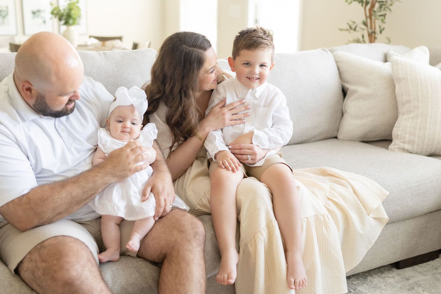 Candid lifestyle photo showing tender family moment on a white couch in bright natural light.