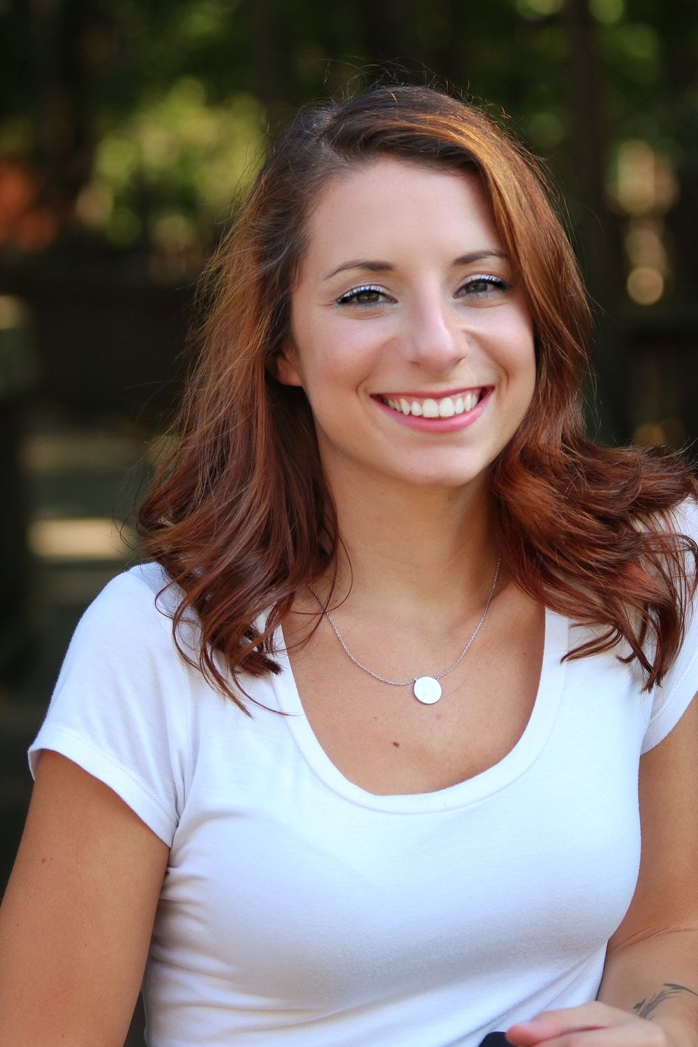 Portrait of a person in a white t-shirt with auburn hair smiling outdoors.