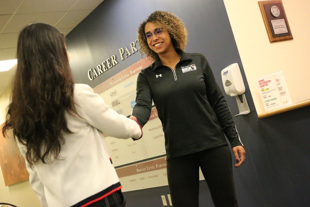 Two people greeting each other with a friendly handshake in an office setting.