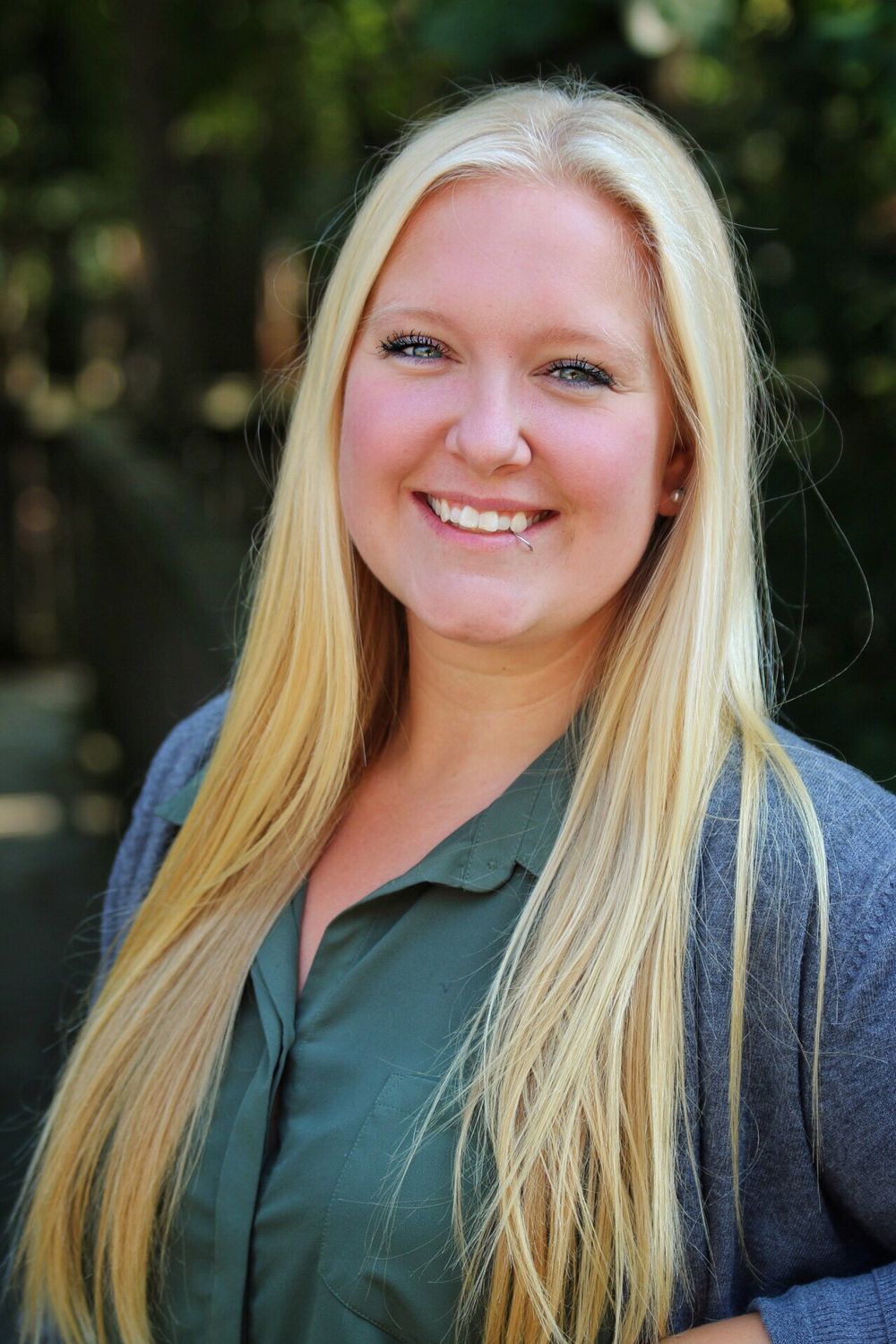 Professional headshot of a person in business attire with long blonde hair against a natural background.