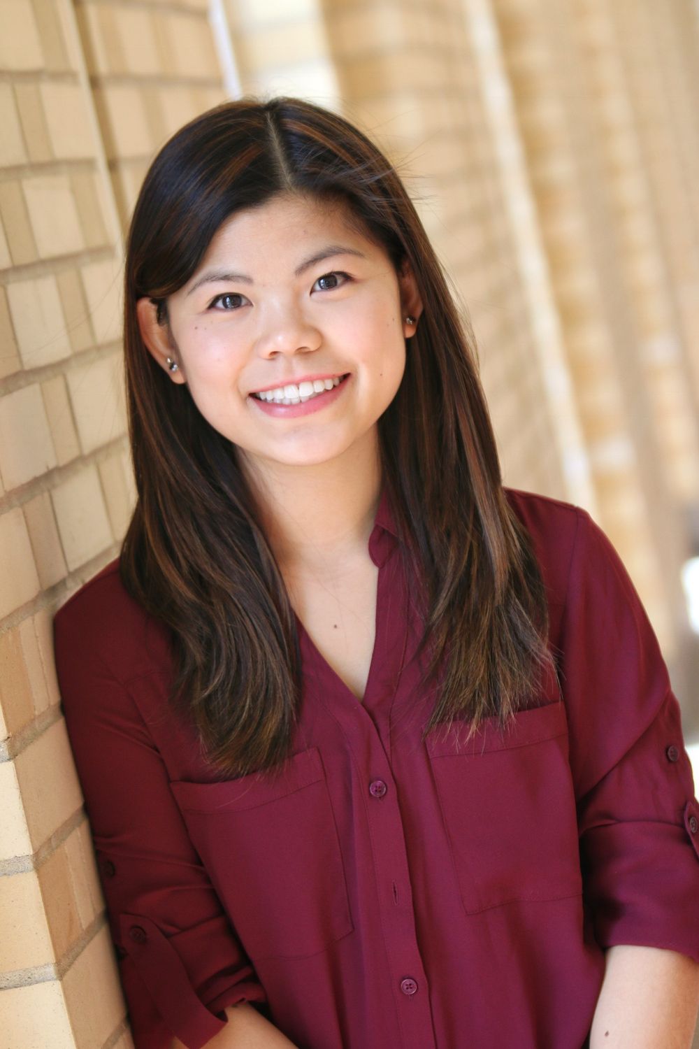 Professional portrait of a person in a burgundy button-down shirt against a brick wall.