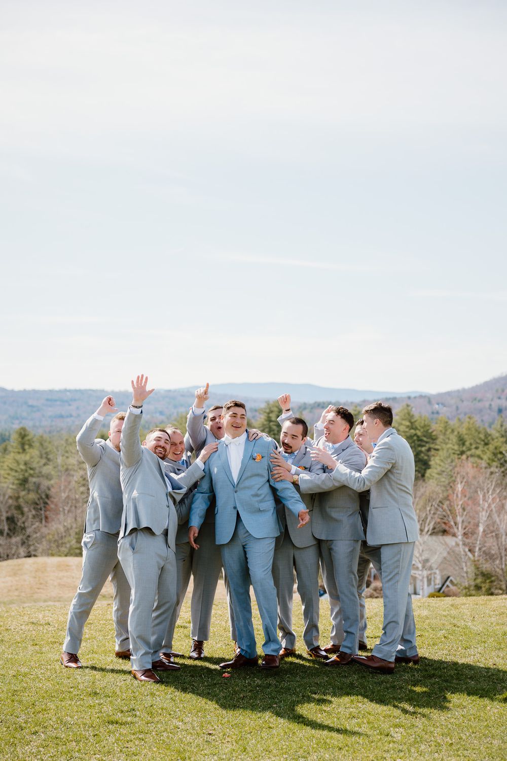 Groomsmen in light blue suits celebrate with the groom outdoors on a sunny day with mountain views.