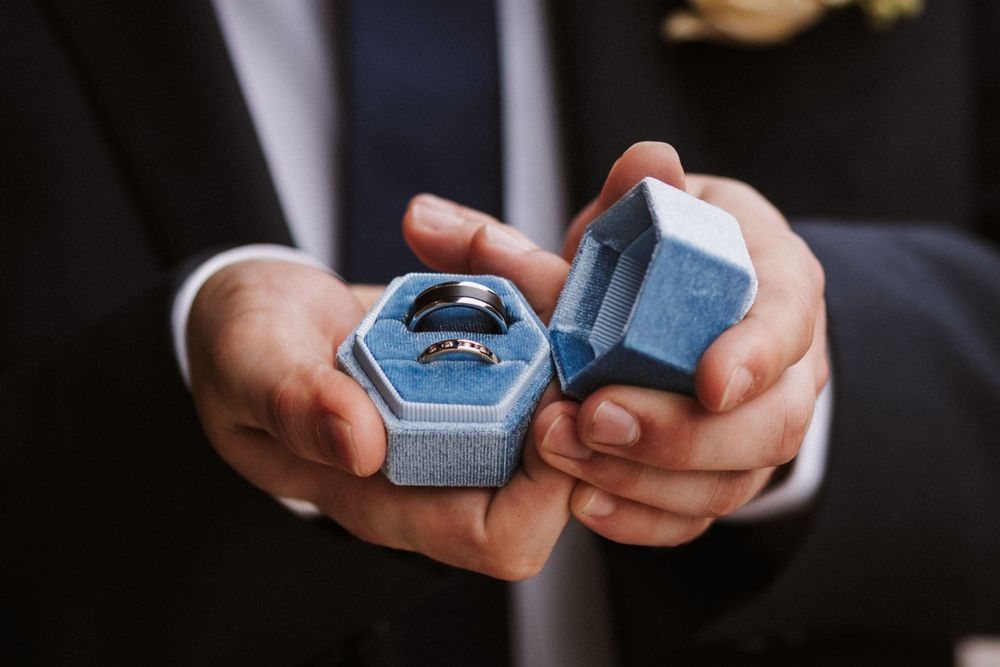 Close-up of hands holding blue velvet ring box with wedding band.