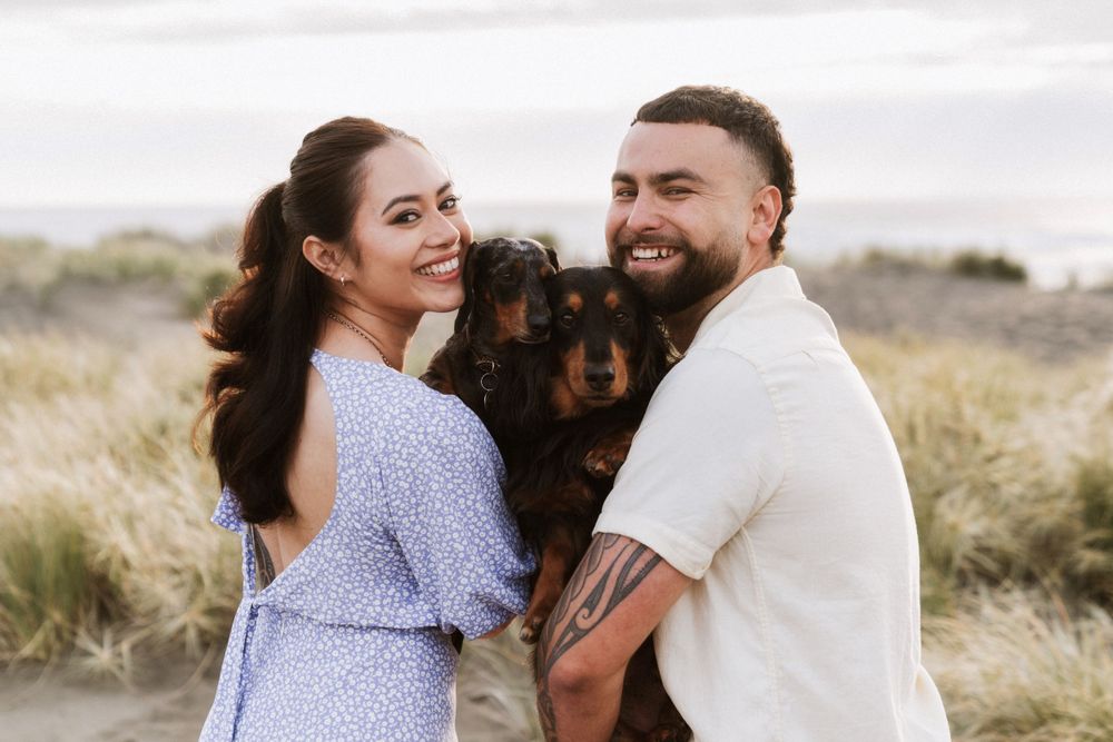 Couple shares intimate moment with their dog in beach during golden hour photo session.