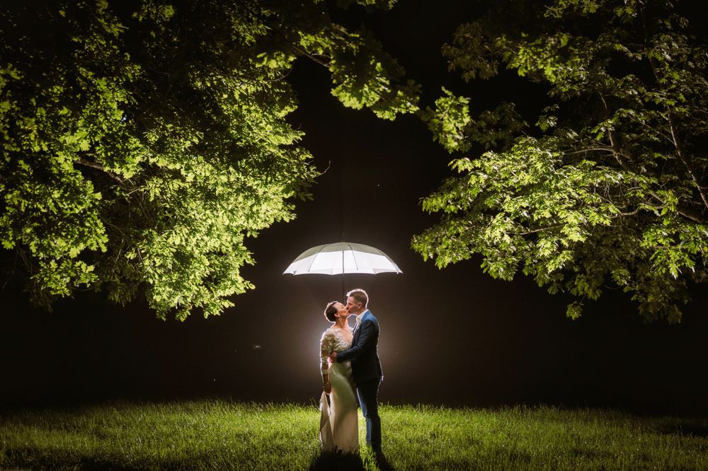 Dramatic nighttime wedding portrait with illuminated umbrella framed by glowing tree canopy.