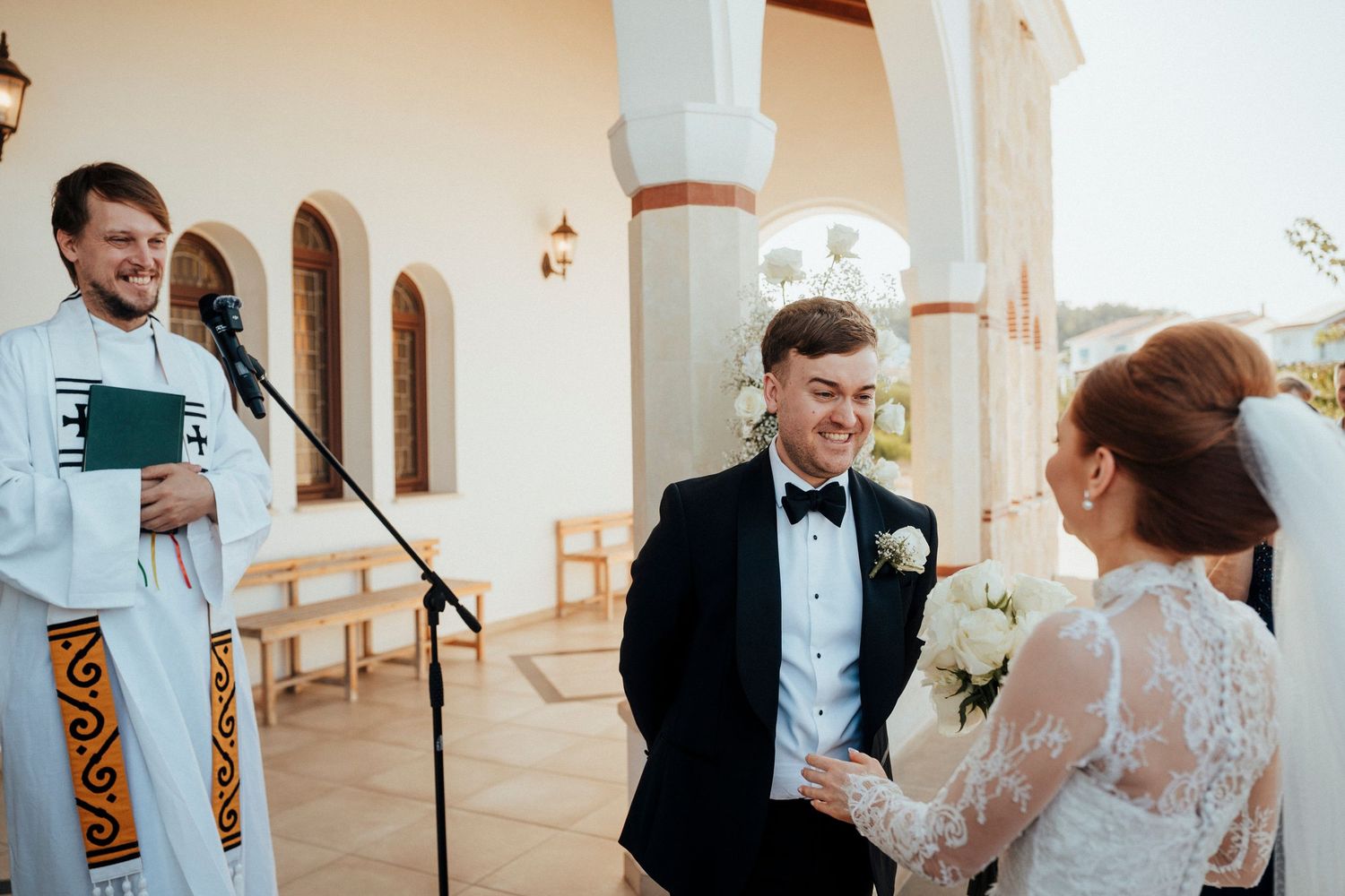 Black and white portrait of a joyful groom laughing during outdoor wedding ceremony.