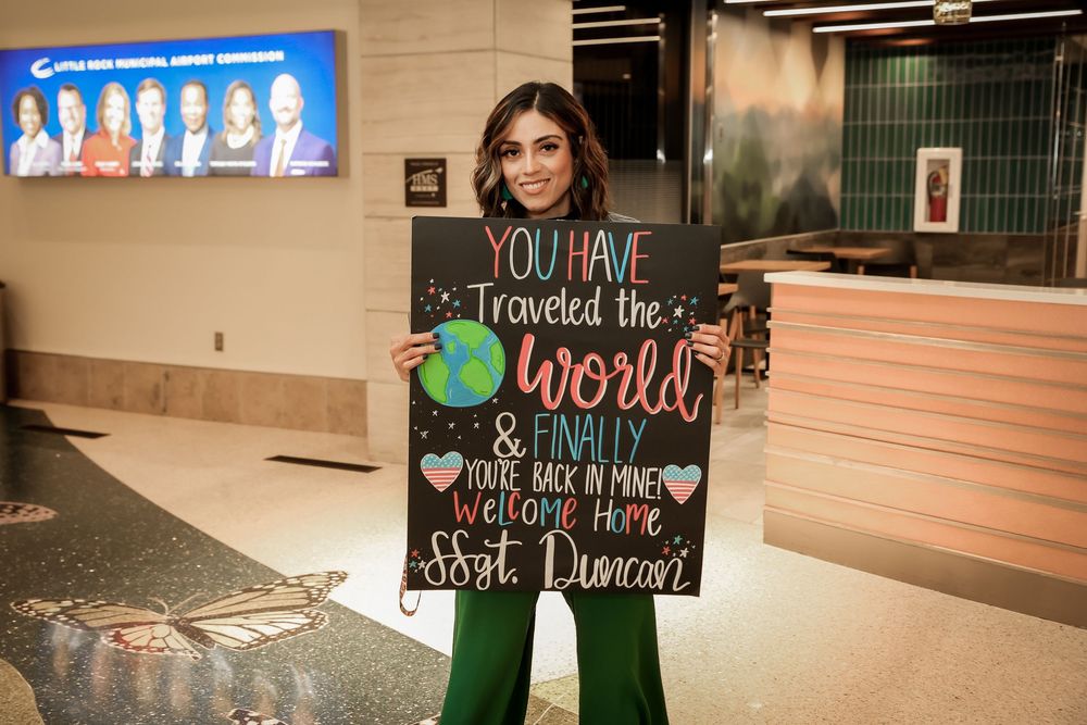 A young woman holds a welcome home sign for Ssgt. Duncan at an airport arrival terminal.