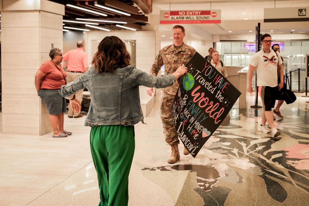 A woman rushes to greet a returning soldier in military uniform at an airport terminal.