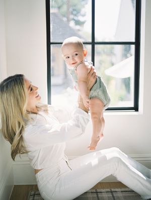 A tender moment between parent and baby by a sunlit window in a bright white room.