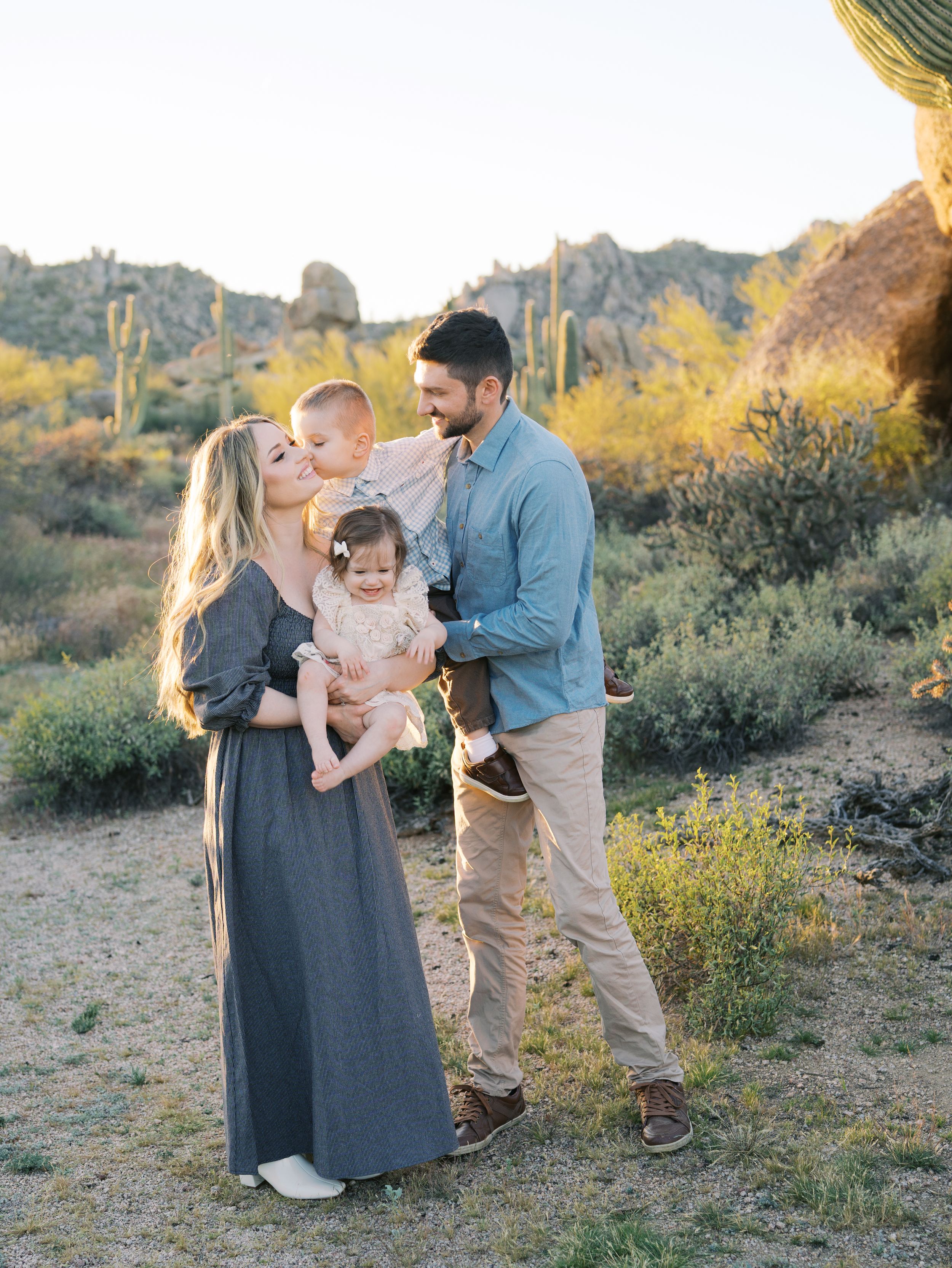 Family shares tender moments together in desert landscape during golden hour photo session.