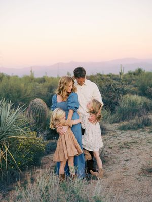 A family stands together in a desert landscape with saguaro cacti and mountains during sunset.