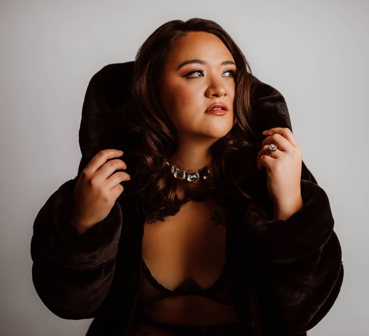 Boudoir editorial photos of a woman wearing a black fur coat, lace bralette with chain necklace, and who poses confidently.