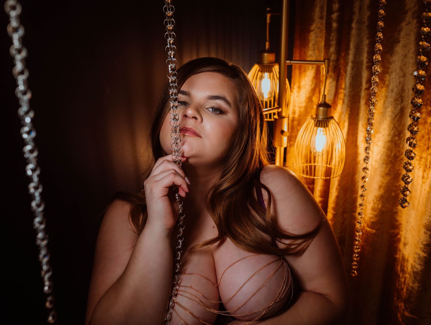 Boudoir by KJ using a moody portrait session in dim lighting with hanging bulbs creating a warm atmospheric glow in the background.
