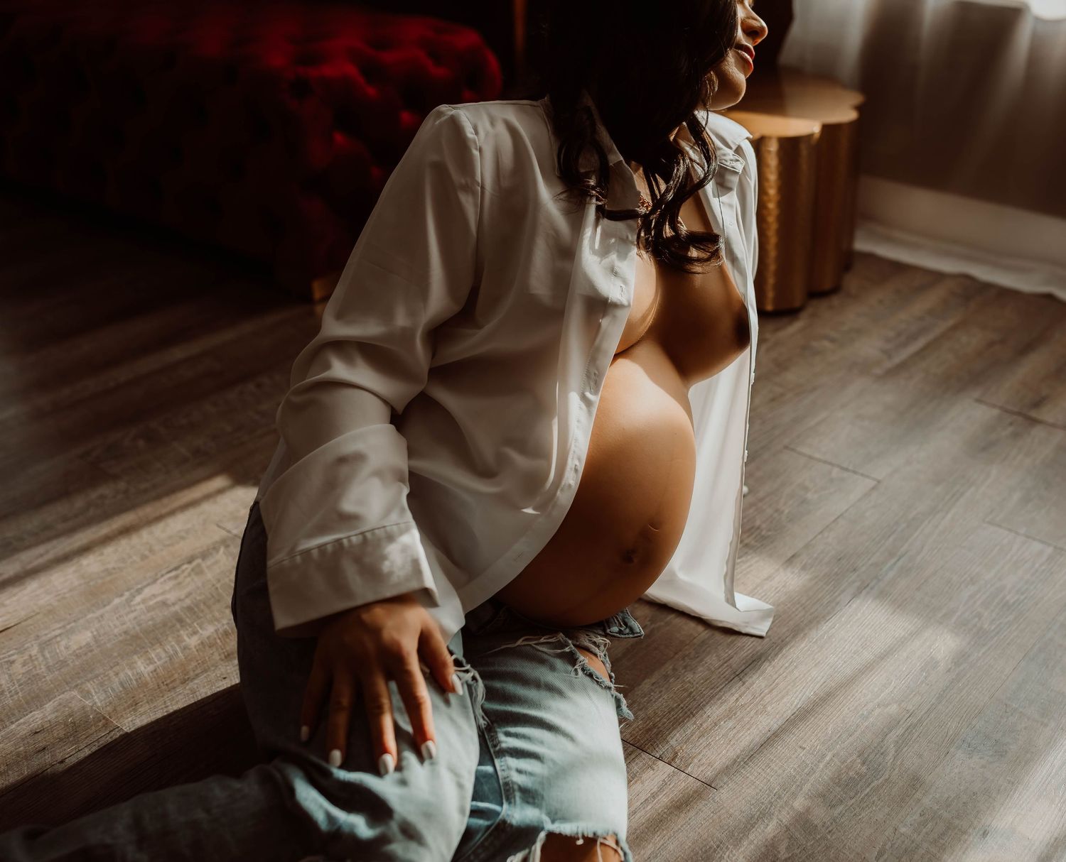 Maternity boudoir with Boudoir by KJ in white button up and jeans sitting on hardwood floor in warm sunlight.