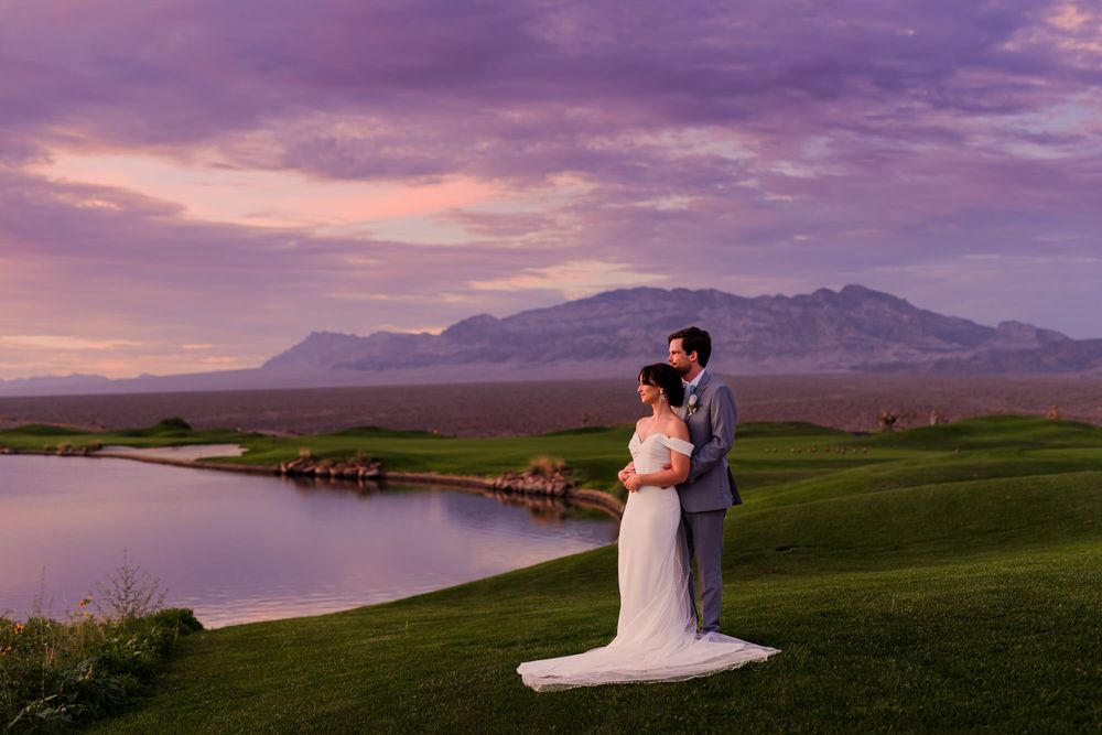 Rolling hills and mountains under a purple sunset sky with a scenic lake view.