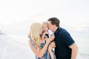 Family sharing a tender moment together on white sandy beach.