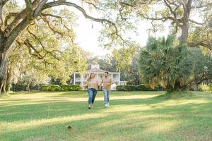 Scenic park landscape with Spanish moss hanging from oak trees and people walking on a grassy path in the distance.