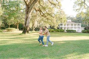 Romantic couple strolling and dancing together on a sunny lawn with Spanish moss draped oak trees and a mansion backdrop.