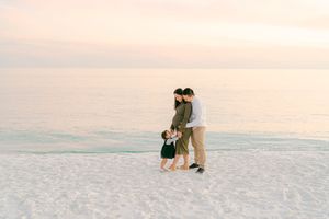 A couple walks along a pristine white sandy beach at sunset with calm ocean waters in the background.