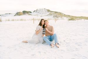 A couple relaxes together on a pristine white sand beach during a romantic photoshoot at sunset.