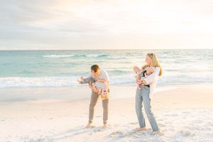 Family enjoying a sunset moment together on a white sandy beach with turquoise ocean waves in the background.