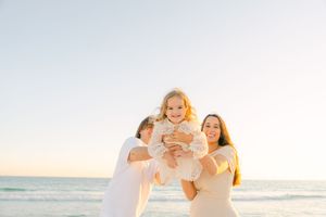 Family enjoys a playful moment together while walking along a sunny beach at sunset.