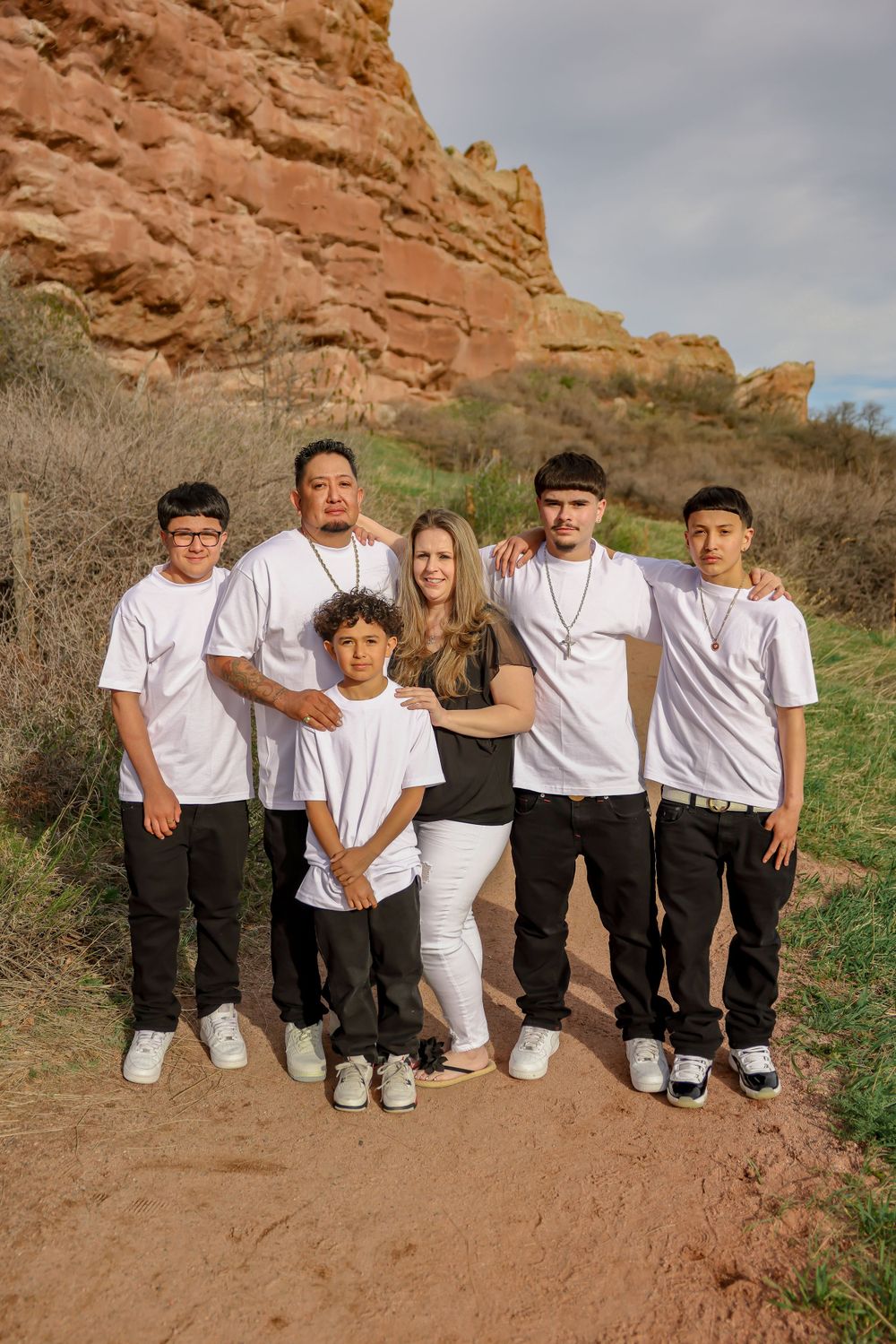 A family wearing matching white t-shirts poses together in front of scenic red rock formations.