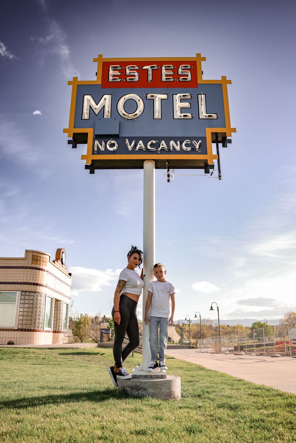 Standing beneath vintage Estes Motel sign with 'No Vacancy' text against blue sky.