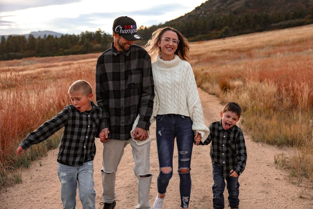 A family of four walks together on a dirt path through a scenic autumn landscape.