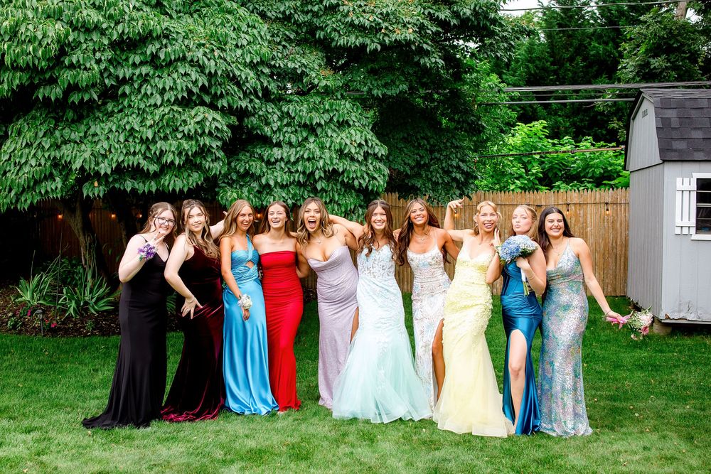 A large group of people in formal attire pose together in a backyard garden setting for a special occasion.