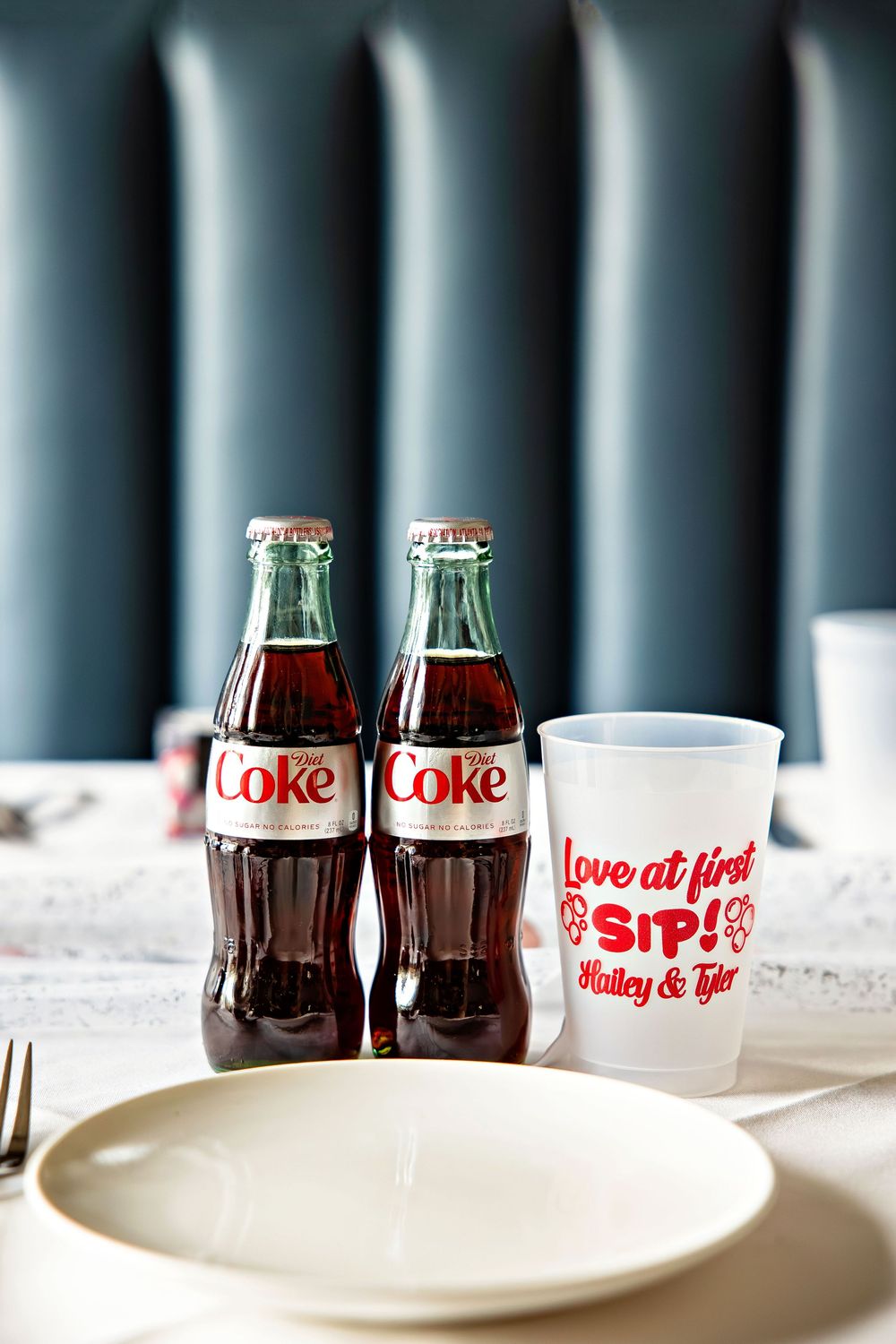 Two Diet Coke bottles beside a personalized wedding cup reading Love at First Sip Hailey and Tyler on a table.