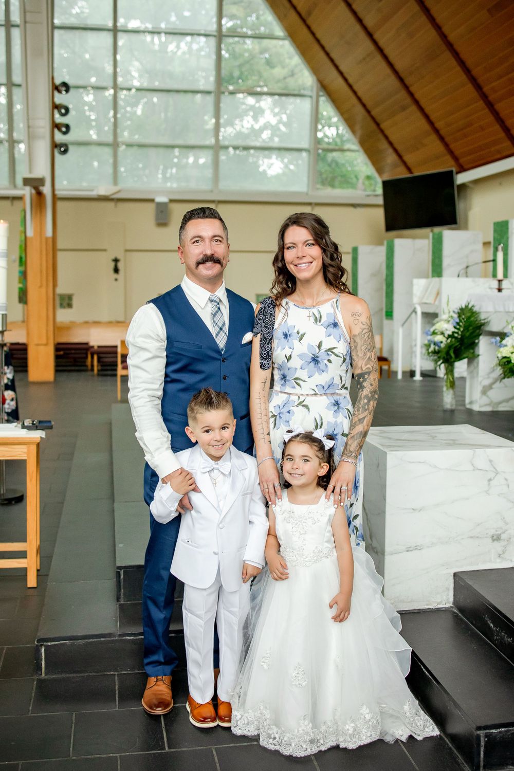 A formal family portrait showing parents and two children dressed elegantly inside a modern venue.